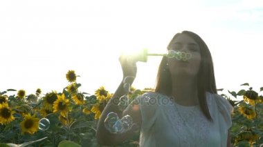 Güzel genç kız ayçiçeği sarı alanına yürüyor ve sabun köpüğü darbeler.