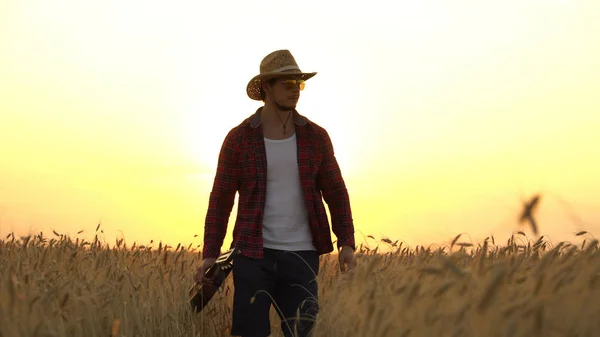 Junger Mann spaziert im Sonnenuntergang über das goldene Weizenfeld und spielt Gitarre. — Stockfoto