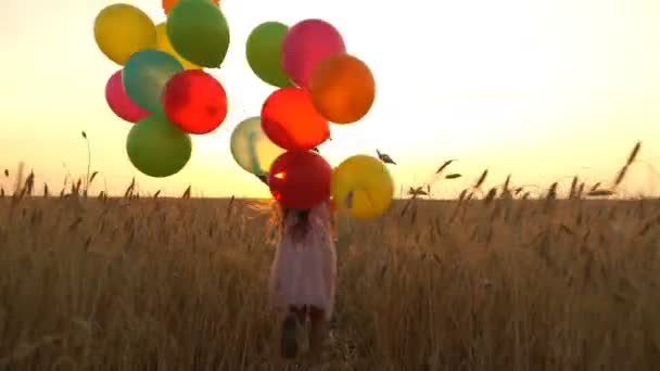 Chica joven en el vestido con globos de colores se ejecuta a través del campo . — Vídeos de Stock