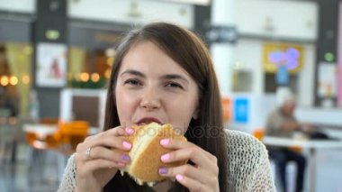 Kız bir food court bir hamburger yiyor.