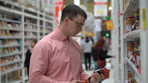 young guy chooses jam in a store or supermarket.