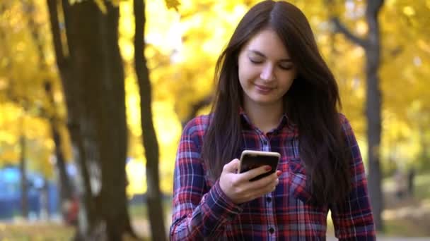 Κορίτσι βόλτες στο πάρκο το φθινόπωρο και χρησιμοποιεί την εφαρμογή στο smartphone σε — Αρχείο Βίντεο