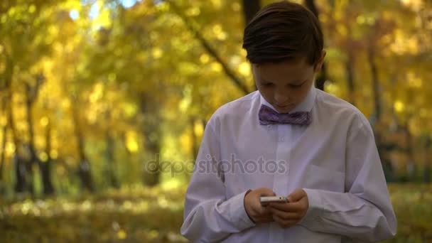 Giovane ragazzo che gioca al telefono e passeggia nel parco autunnale — Video Stock