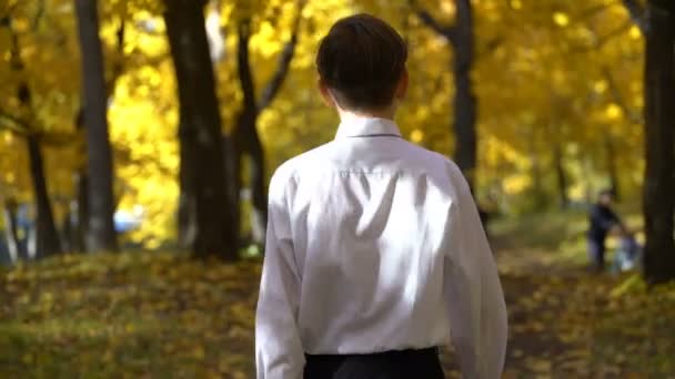 Ο νεαρός άντρας σε ένα άσπρο shirtwalks στο πάρκο φθινόπωρο — Αρχείο Βίντεο