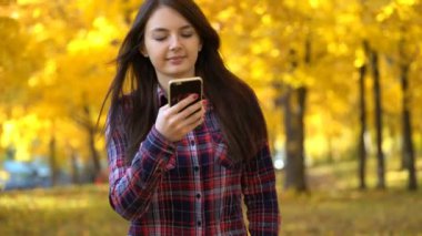 Kız parkta sonbaharda yürür ve onun smartphone uygulama kullanır