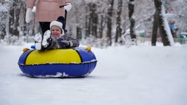 Zweijähriger Junge rollt im Winter auf Schläuchen im Park. — Stockvideo