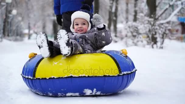 Zweijähriger Junge rollt im Winter auf Schläuchen im Park. — Stockvideo