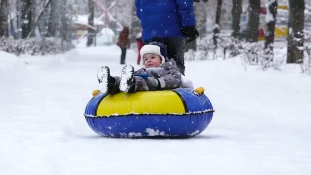 Zweijähriger Junge rollt im Winter auf Schläuchen im Park. — Stockvideo