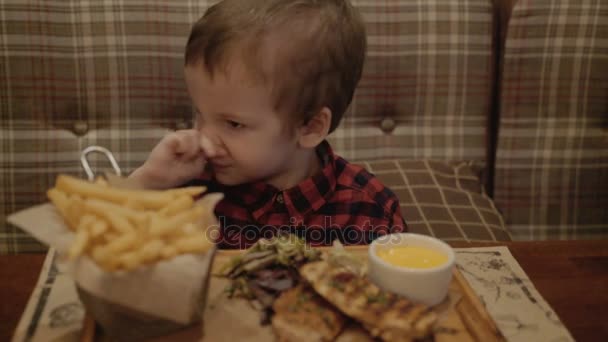 Pojke på två år är att äta pommes frites i en restaurang. — Stockvideo