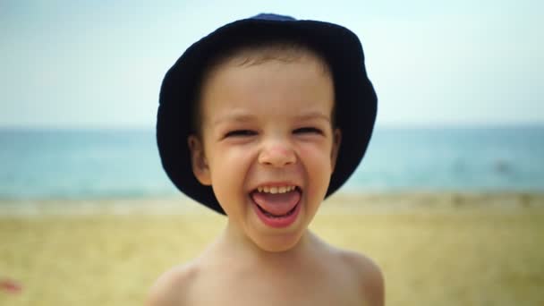Jongen van twee jaar voor de gek houden door een camera op het strand in de buurt van de Oceaan. — Stockvideo