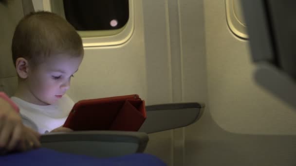 Pojke två år gammal spelar på en tablet-app, och sitta i en stol i flygplanet. — Stockvideo
