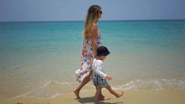 Mãe e filho caminhando a pé ao longo da praia perto do oceano . — Fotografia de Stock