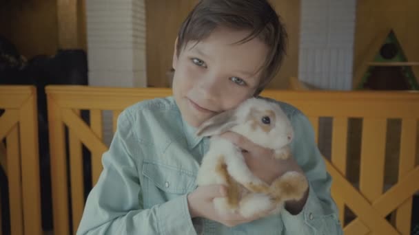 Αγόρι ένα κουνέλι κρατά στα χέρια του σε ένα αγρόκτημα. — Αρχείο Βίντεο