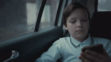 Sosyal ağ üstünde onun smartphone kullanarak yağmurlu gün boyunca şehirde Araba sürme üzgün, mutsuz genç çocuk
