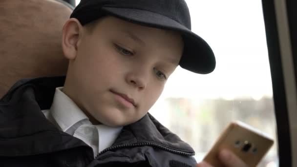 Nahaufnahme eines kleinen Jungen, der mit dem Bus durch die Stadt fährt. er mit dem Smartphone. — Stockvideo
