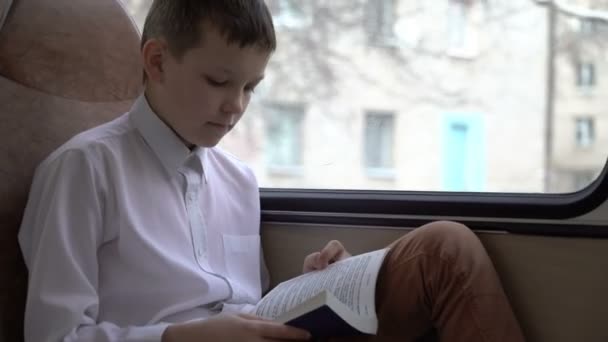 Skott av ung skolpojke resor med buss genom staden och läser en bok. — Stockvideo