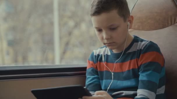 Primer plano de un niño viajando en autobús a través de la ciudad, utilizando la red social en su tableta de ordenador . — Vídeo de stock