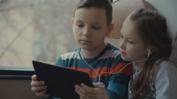 Close-up shot of a young boy and girl traveling by bus through city, watching movie on computer tablet. — Stock Video