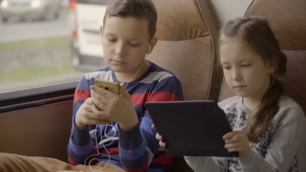 Close-up shot of a young boy and girl traveling by bus through city, using social network at their gadgets. — Stock Video