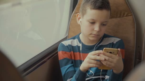 Nahaufnahme eines kleinen Jungen, der mit dem Bus durch die Stadt fährt. er nutzt das soziale Netzwerk auf seinem Smartphone und hört Musik. — Stockvideo