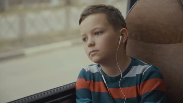 Primer plano de un niño viajando en autobús a través de la ciudad. Escucha música. . — Vídeo de stock