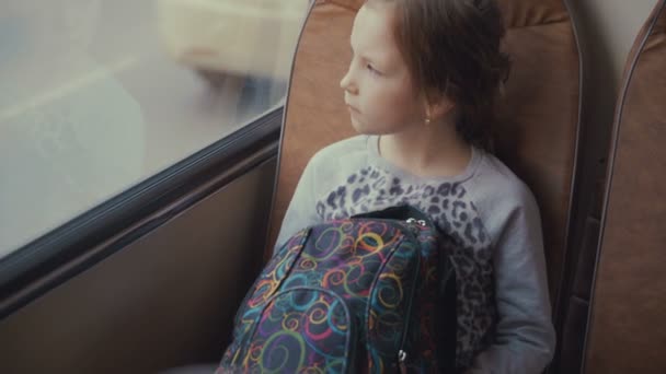 Jeune, belle fille passager avec sac d'école dans le bus scolaire en mouvement regardant par la fenêtre . — Video