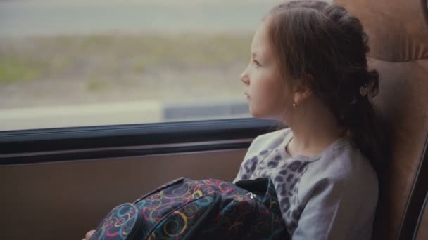 Giovane, bella ragazza passeggera con borsa scolastica nel bus scolastico in movimento guardando fuori dal finestrino . — Video Stock