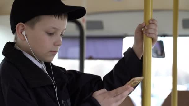 特写镜头, 一个年轻的男孩乘公交车穿过城市。他使用智能手机和听音乐. — 图库视频影像