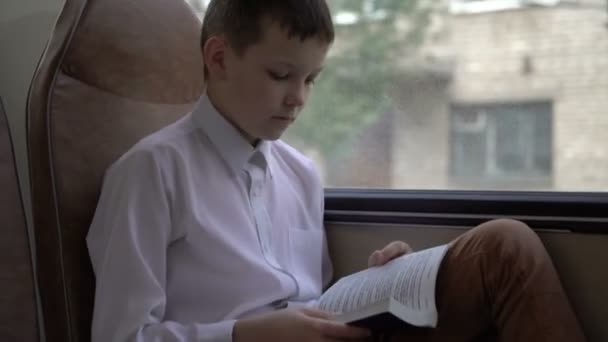 Aufnahme eines jungen Schülers, der mit dem Bus durch die Stadt fährt und ein Buch liest. — Stockvideo