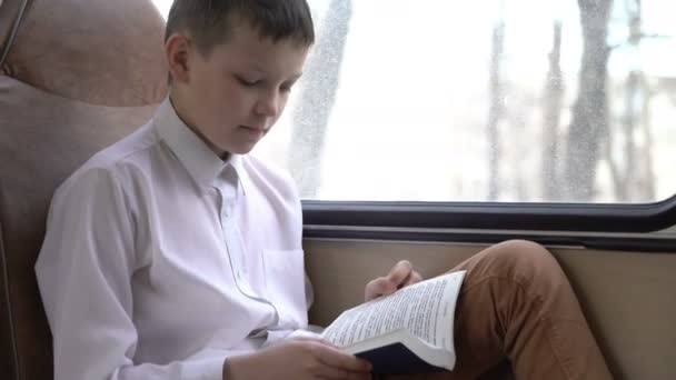 一个年轻的小学生乘坐公交车穿过城市, 读了一本书的照片. — 图库视频影像
