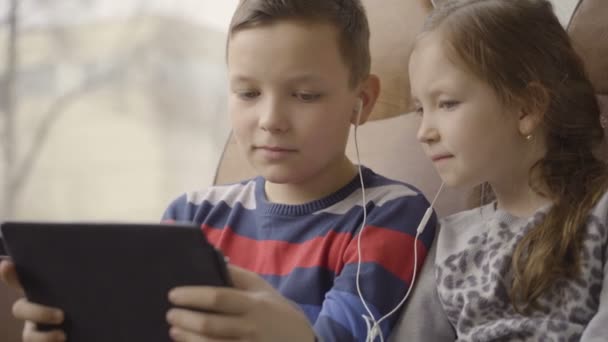 Close-up shot of a young boy and girl traveling by bus through city, watching movie on computer tablet. — Stock Video