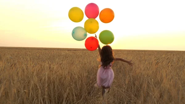 Mädchen läuft mit Luftballons auf einem Feld — Stockfoto