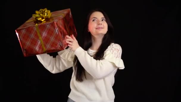 Mujer joven con una caja de regalo sobre fondo negro. caja de regalo con cinta blanca para Feliz Año Nuevo, Feliz Navidad, Día de San Valentín, cumpleaños . — Vídeo de stock