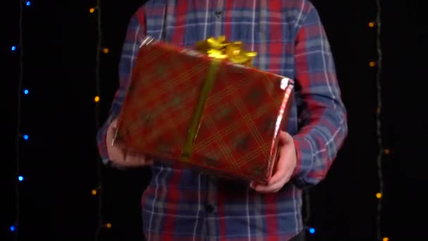 Junge mit einem Geschenkkarton auf schwarzem Hintergrund. Geschenkbox mit Schleife für ein frohes neues Jahr, frohe Weihnachten, Valentinstag, Geburtstag — Stockvideo