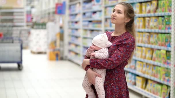 Kadın süpermarket alışverişi sırasında elinde küçük bir kız çocuğu olan çocuk maması seçiyor. — Stok video