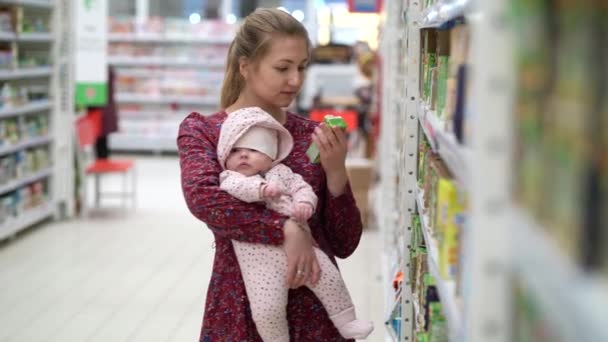 Mujer la elección de los niños alimentos con el bebé niña pequeña en las manos durante las compras del supermercado — Vídeos de Stock
