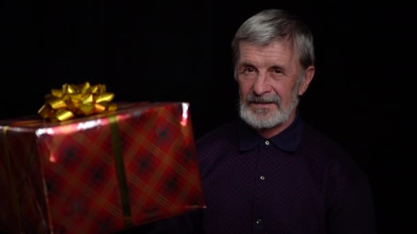 Sorrindo homem idoso feliz com uma caixa de presente no fundo preto . — Vídeo de Stock