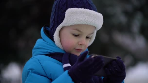 Little boy in winter wear using phone on cold snowy day — Stock Video