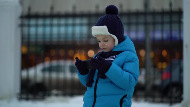 Liten pojke på vintern bära med hjälp av telefon på kall snöig dag — Stockvideo