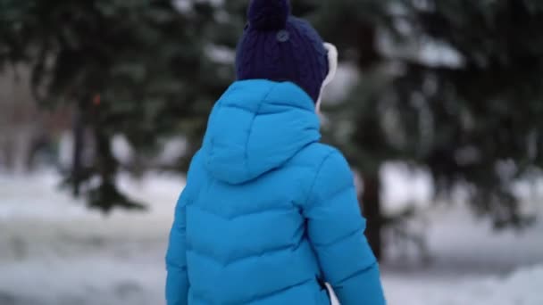 Aranyos négy éves fiú kék téli ruhákban sétál a havas utcán. — Stock videók