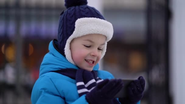Kleine jongen in de winter dragen met behulp van telefoon op koude besneeuwde dag — Stockvideo