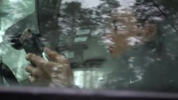 若い男が車の中でスマートフォンを使っている。彼はチャット、ニュースをオンラインでチェックしている — ストック動画