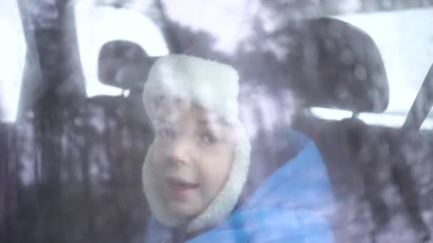 Little boy rides in the car in the back seat in winter forest and looks out the window — 비디오