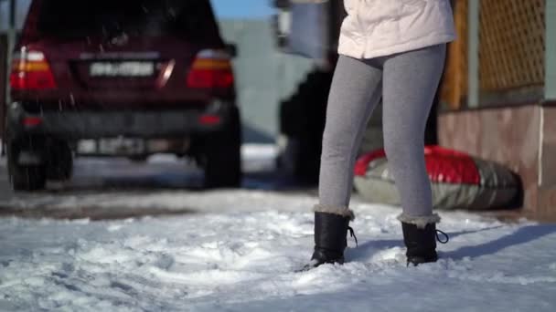 Ung kvinna skotta snö på bakgården nära huset . — Stockvideo