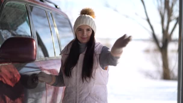 Jonge vrouw staat in de buurt van een auto en zwaaide zijn hand naar de camera in de winter. — Stockvideo