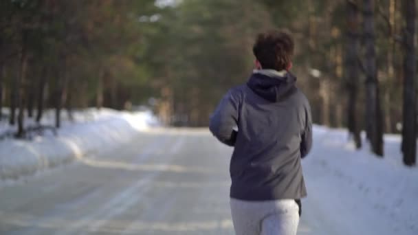 Молодой спортсмен бегает в зимнем лесу — стоковое видео