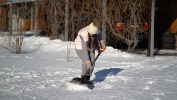 Jeune femme pelletant la neige sur la cour près de la maison  . — Video