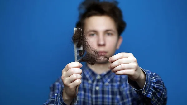 Ung man dra kluster av hår från en kam till följd av håravfall — Stockfoto