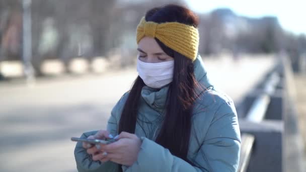 Молодая женщина в маске смс на смартфоне — стоковое видео
