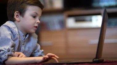 Mavi tişörtlü bebek tabletten izliyor.